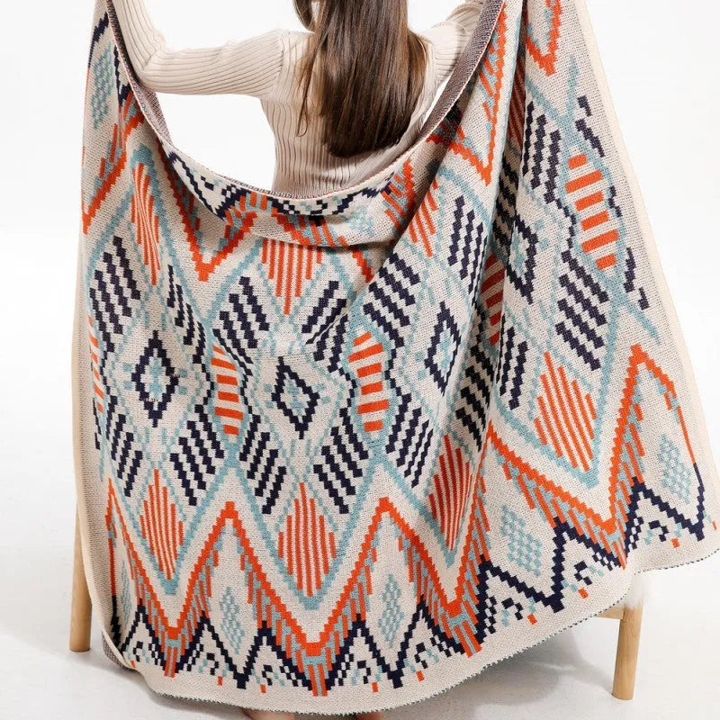 Beige and orange bohemian-style acrylic sofa blanket with tassel fringe on a grey sofa.