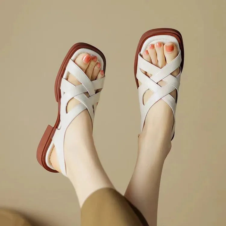 Women's black patent leather square toe sandals with cross straps on a low rubber sole.