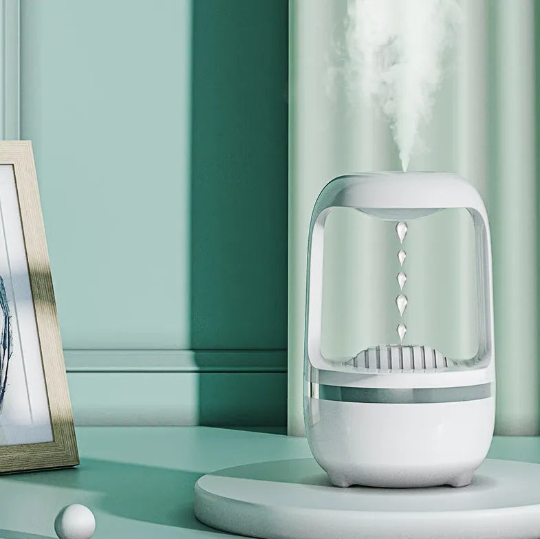 White anti-gravity water droplet humidifier on a wooden desk with visible mist and upward-flowing water beads.