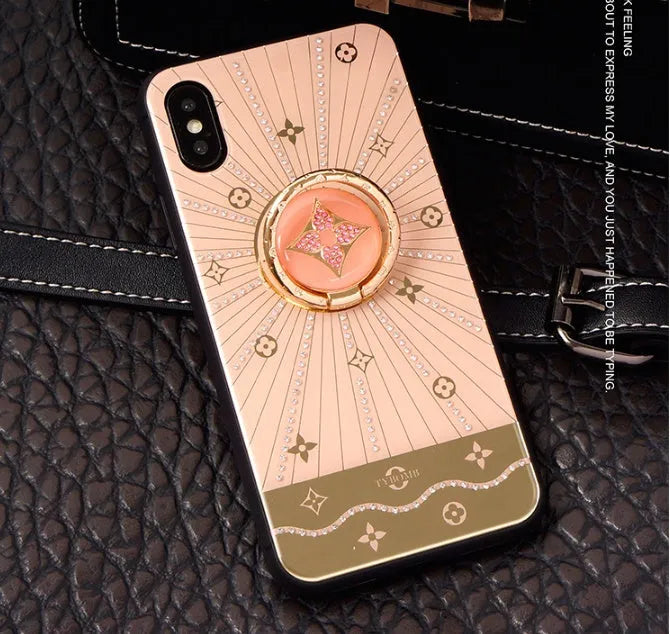 Gold-tone phone stand with diamond crystals holding iPhone and rings