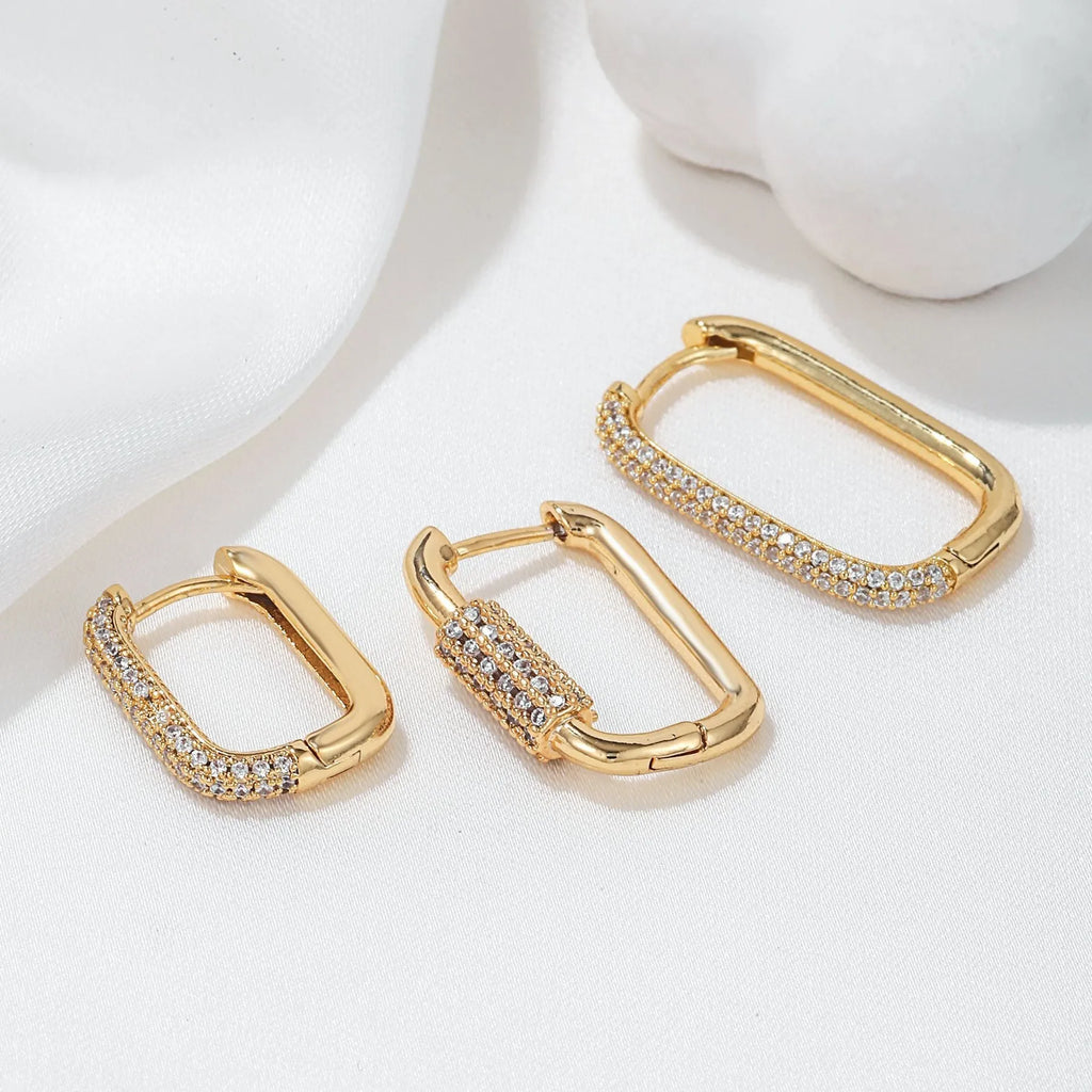 Three geometric square ear clips with inlaid zircon details in gold and white finishes on a grey background.