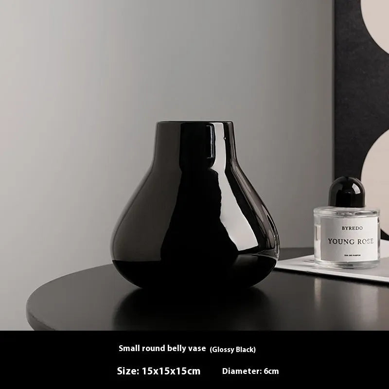 Ceramic round belly vase in black or white with artificial orchid stems on wooden surface