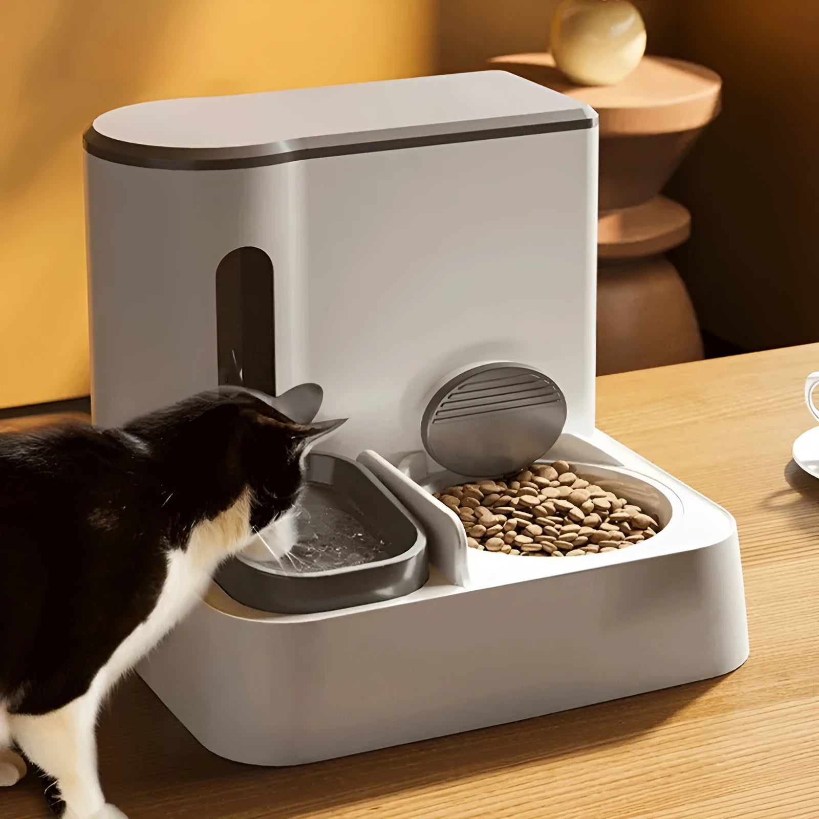 Grey automatic cat feeder and water dispenser station with integrated double bowls on a wooden floor.
