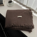 Four-layer gauze cotton tassel blanket in avocado green colour laid flat.