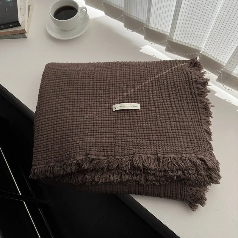 Four-layer gauze cotton tassel blanket in avocado green colour laid flat.