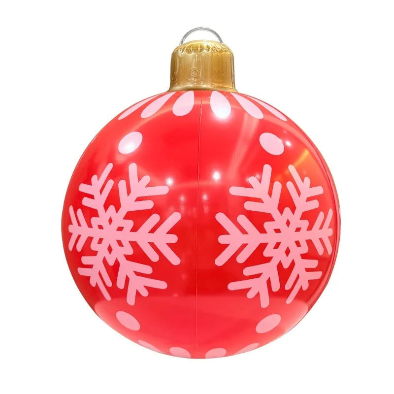 Large red inflatable Christmas ball with snowflake design and flashing LED lights in a garden.