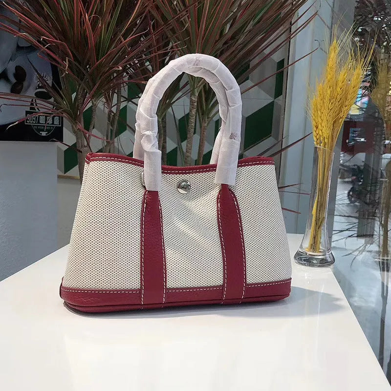 Women's canvas bucket tote bag with leather handles and detailing in black, shown with open top revealing internal zip pocket.