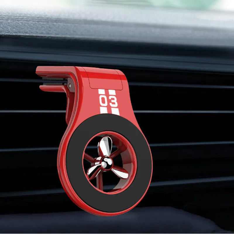 Black magnetic car phone holder clipped to a car air vent, showing a smartphone attached and the included fragrance slice.