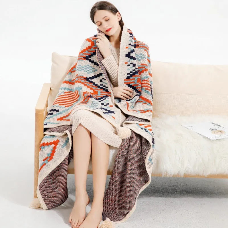 Beige and orange bohemian-style acrylic sofa blanket with tassel fringe on a grey sofa.