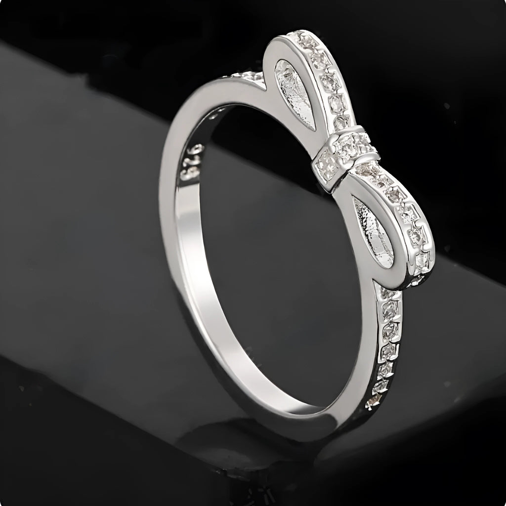 Silver coloured bow-shaped ring with sparkling rhinestone and zircon crystal details on a finger.