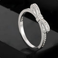 Silver coloured bow-shaped ring with sparkling rhinestone and zircon crystal details on a finger.