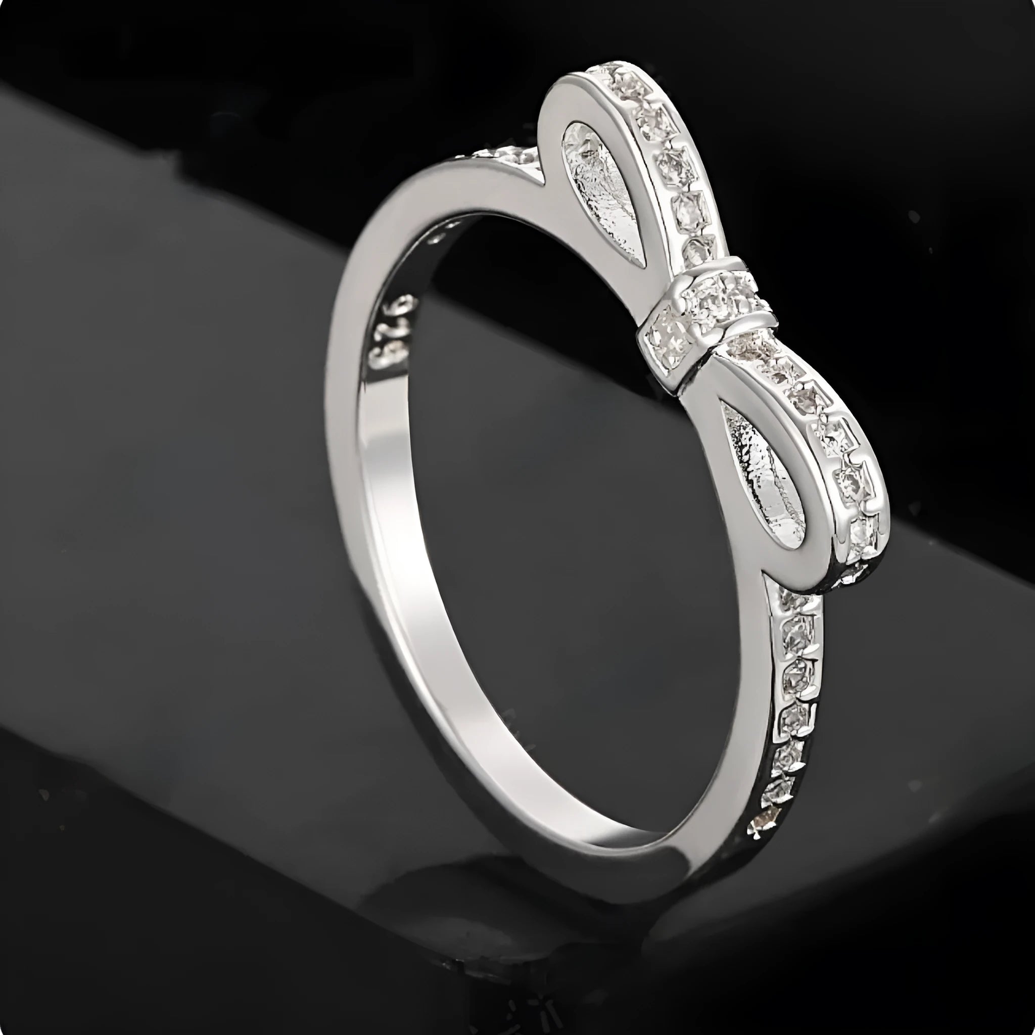 Silver coloured bow-shaped ring with sparkling rhinestone and zircon crystal details on a finger.