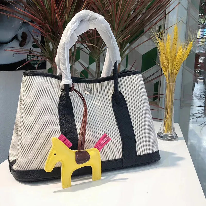 Women's canvas bucket tote bag with leather handles and detailing in black, shown with open top revealing internal zip pocket.