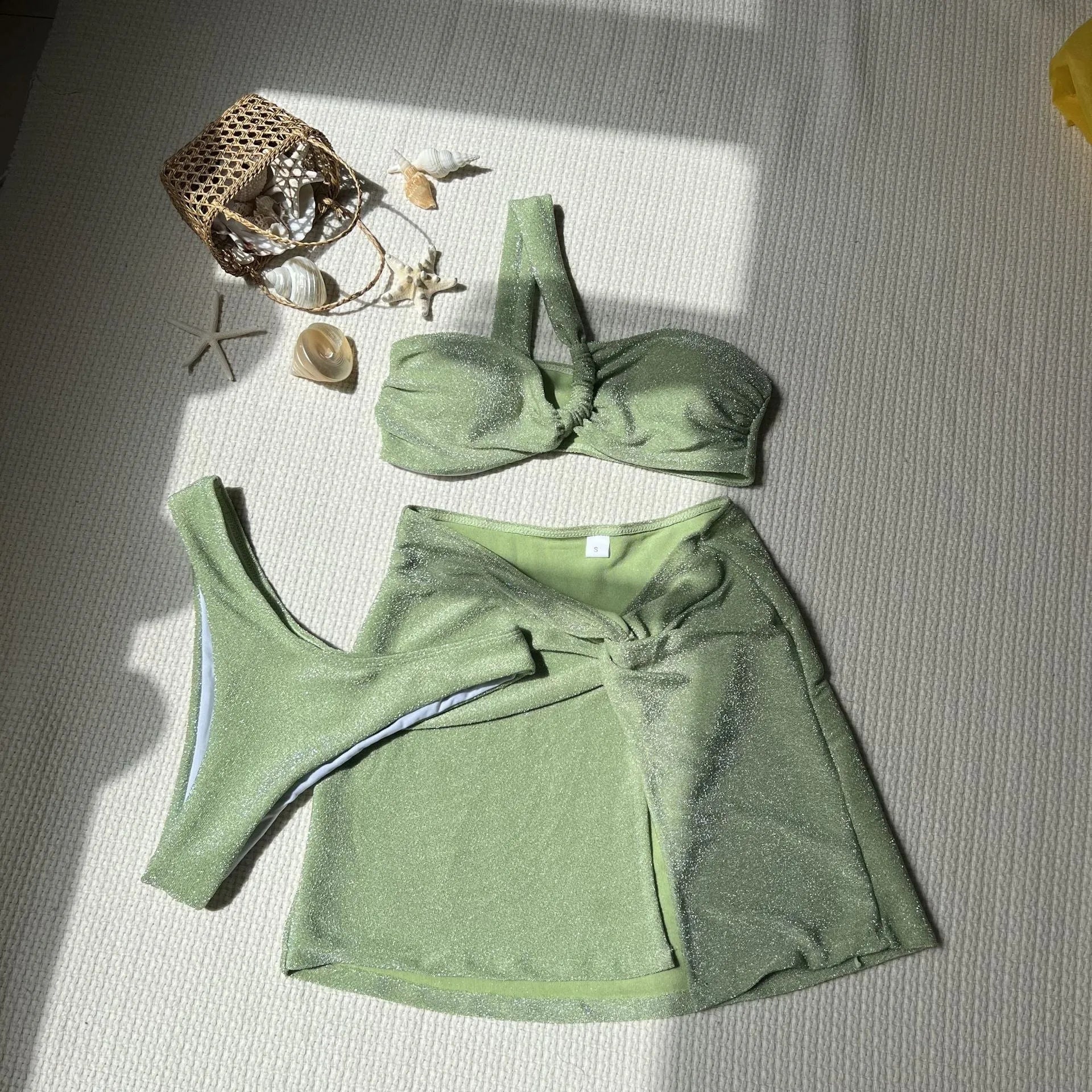 Women's light green one-shoulder swimsuit top with matching briefs and skirt laid flat.