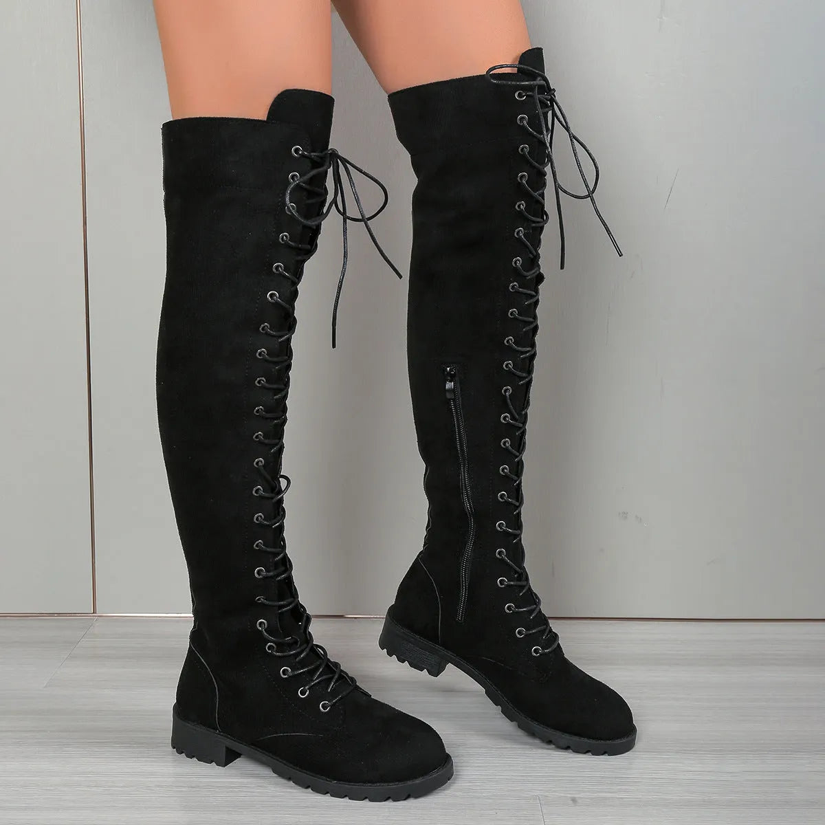 Black lace-up over the knee boots with a round toe and flat rubber sole on a neutral background.