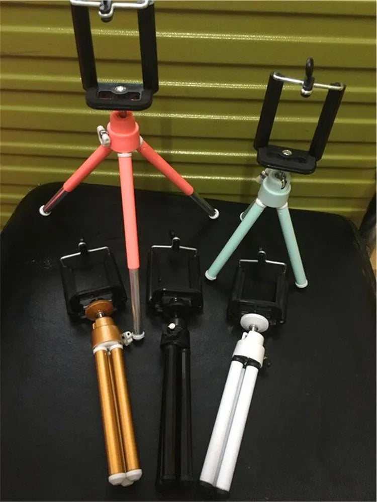 Black metal desktop phone holder with adjustable arm holding a smartphone on a wooden desk.