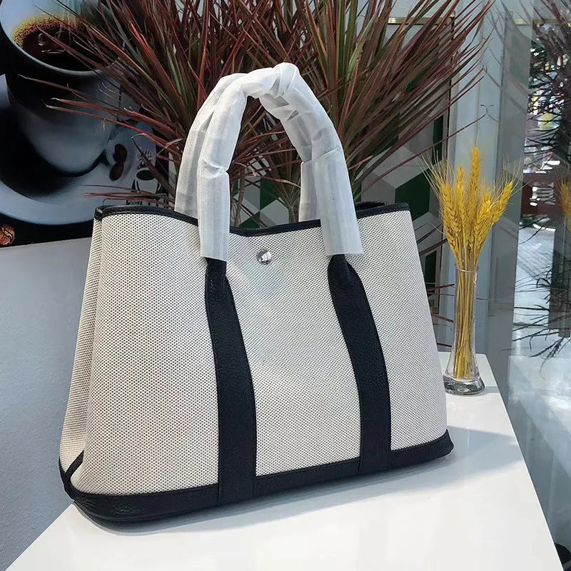 Women's canvas bucket tote bag with leather handles and detailing in black, shown with open top revealing internal zip pocket.