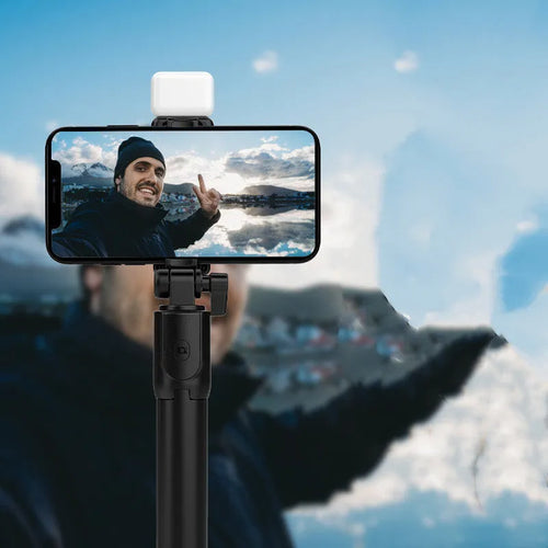 Black aluminium alloy Bluetooth selfie stick with extended tripod legs and a phone attached to the 360-degree rotating holder.