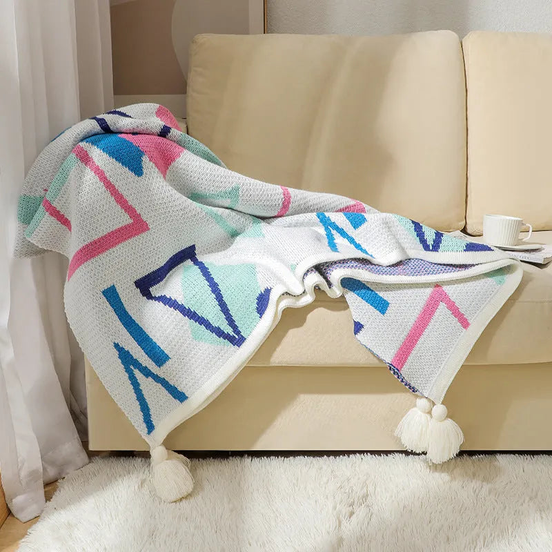 Beige and orange bohemian-style acrylic sofa blanket with tassel fringe on a grey sofa.