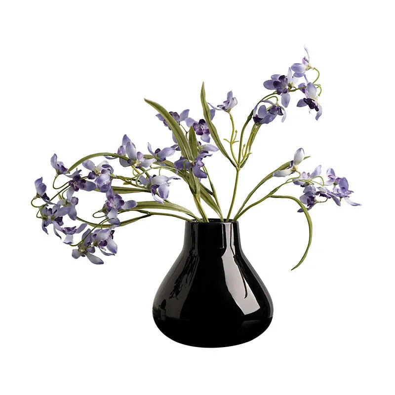 Ceramic round belly vase in black or white with artificial orchid stems on wooden surface