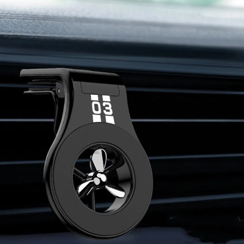 Black magnetic car phone holder clipped to a car air vent, showing a smartphone attached and the included fragrance slice.