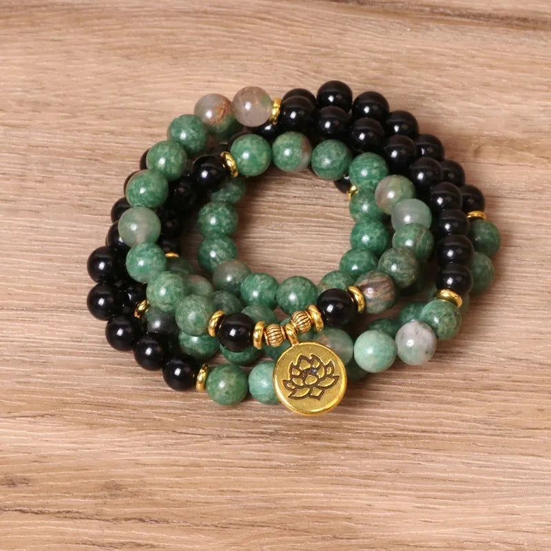 Green and black elastic beaded bracelet with metallic alloy charm details on a wrist.