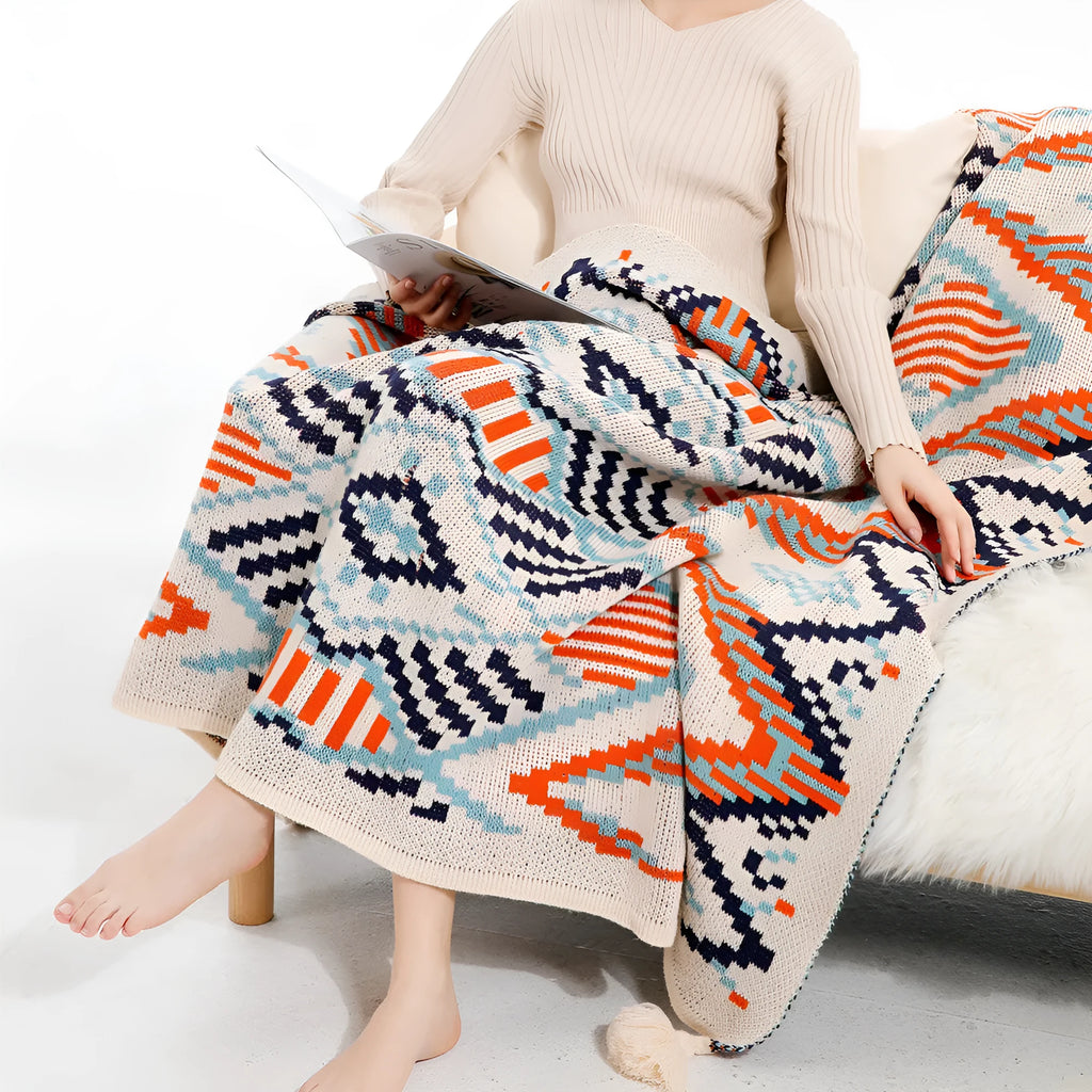 Beige and orange bohemian-style acrylic sofa blanket with tassel fringe on a grey sofa.