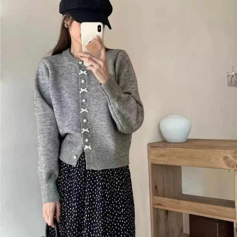 Women's solid colour cashmere cardigan with bow detail and pearl buttons on a hanger