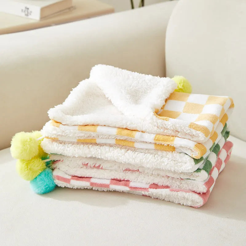 Green plaid pattern pet blanket with fur ball tassels on a sofa.
