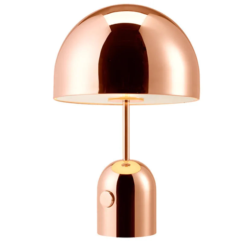 Mushroom shaped metal table lamp in rose gold finish on a wooden surface.