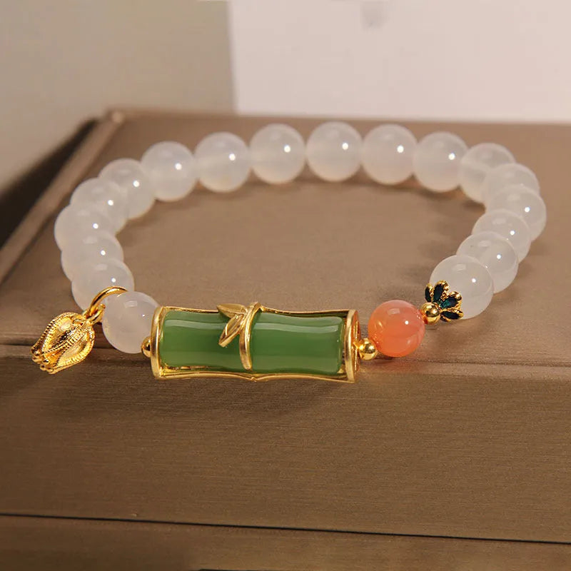 Women's bracelet with white agate bead and bamboo-shaped jade segments on a neutral background.