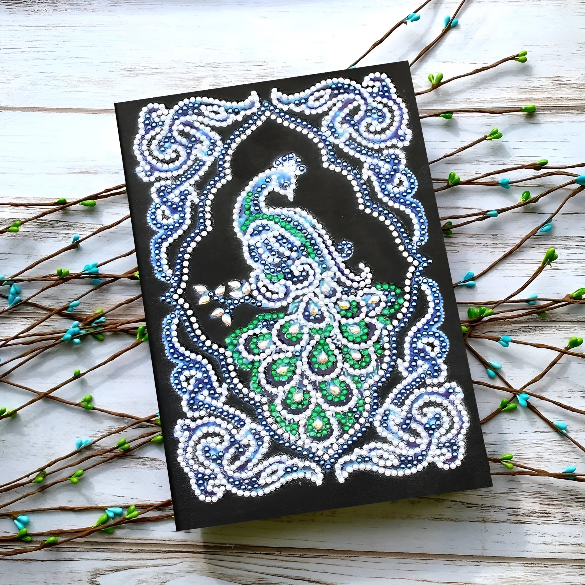 Black A5 diamond painting notebook with a peacock design cover, shown closed.