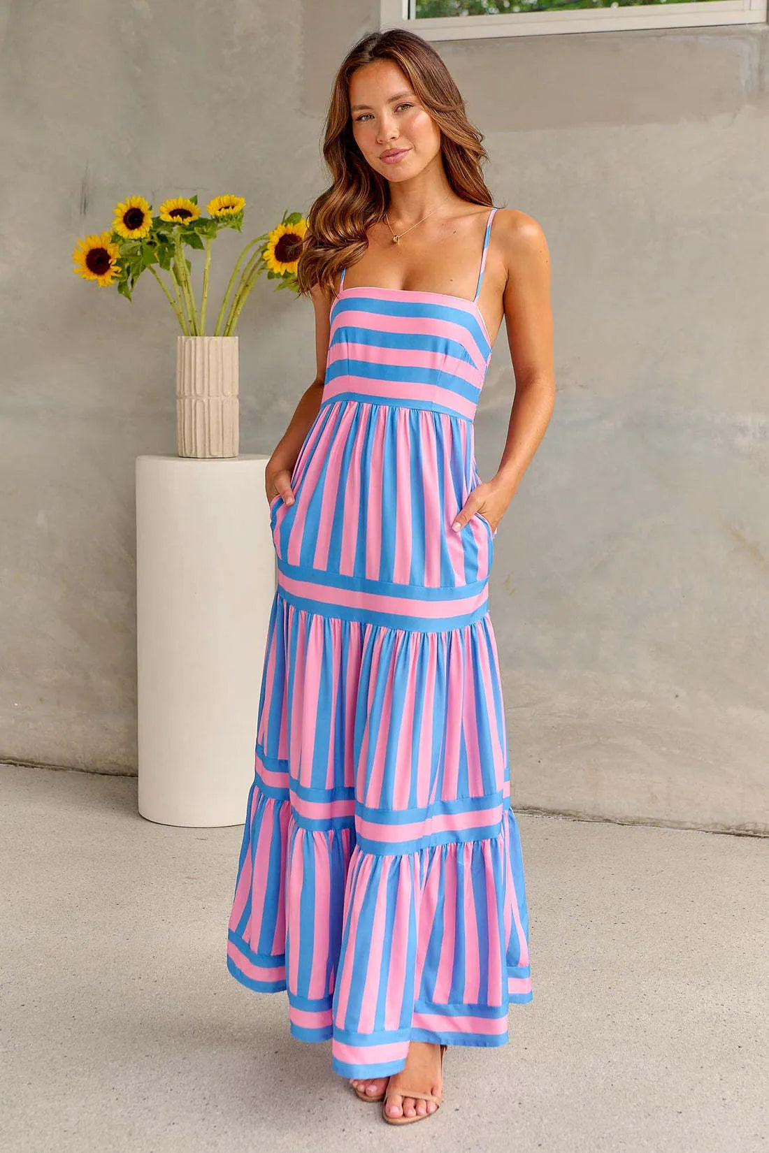 A woman wearing a striped backless suspender summer dress with a square neckline and side pockets.
