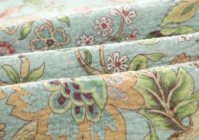 Blue American floral and bird print cotton quilted bedspread set with matching sheet on a bed.