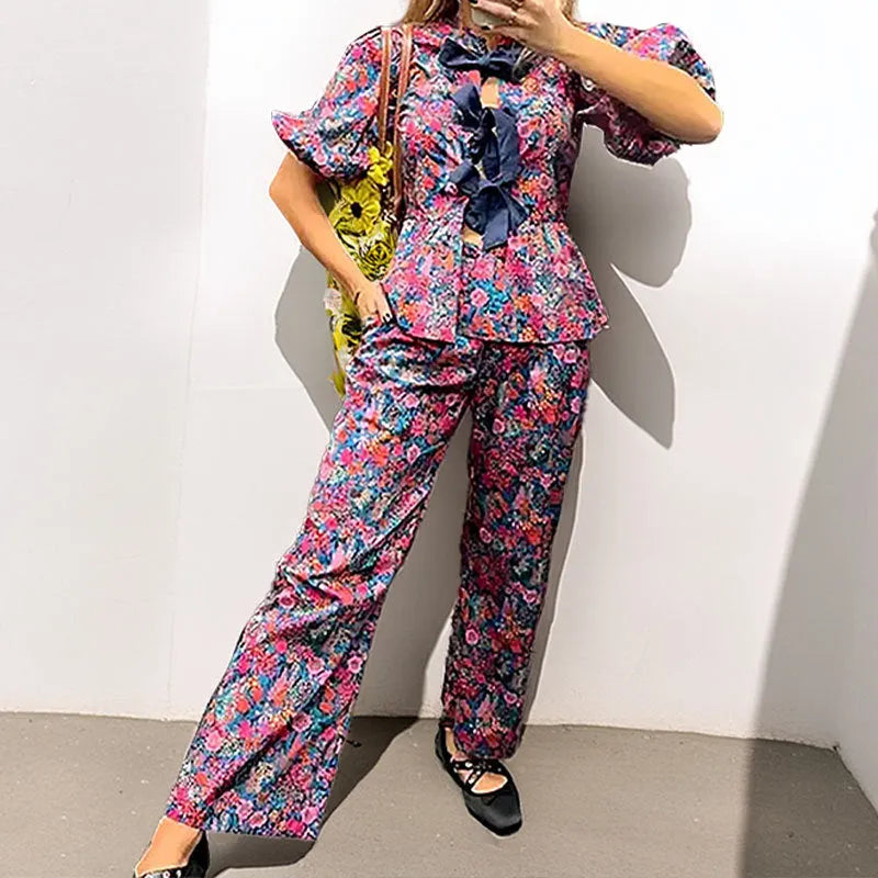 Women's floral print two-piece suit with a tie-neck puff sleeve top and matching trousers.