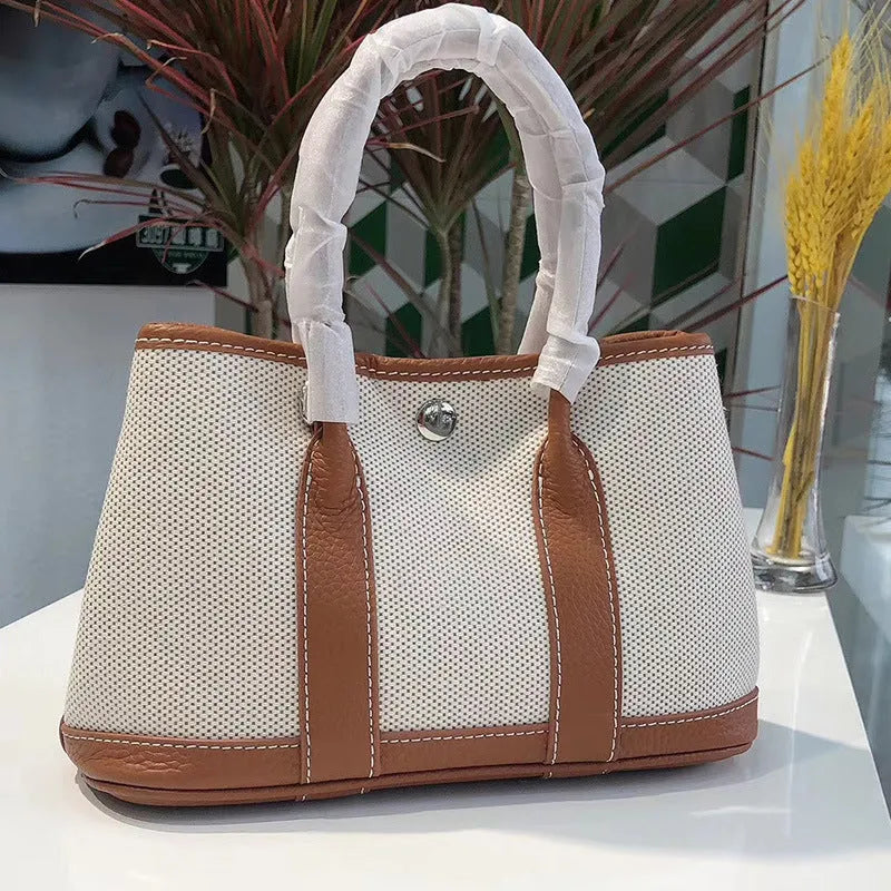 Women's canvas bucket tote bag with leather handles and detailing in black, shown with open top revealing internal zip pocket.