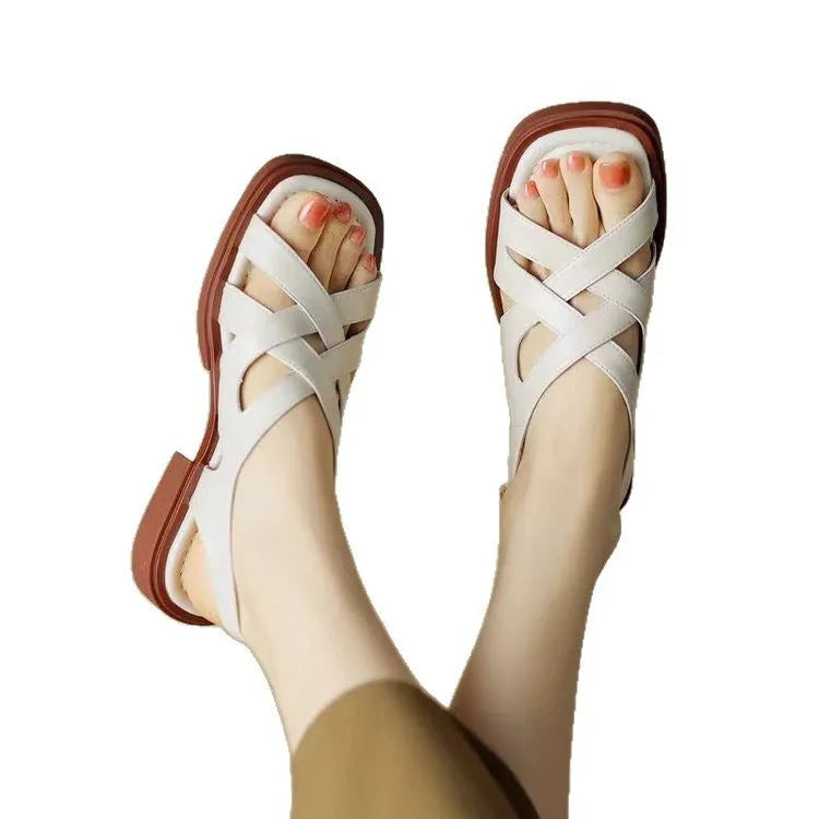 Women's black patent leather square toe sandals with cross straps on a low rubber sole.
