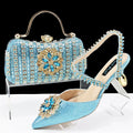 Women's black high heel sandals with ankle chain, floral rhinestone detail, and matching hard clutch bag