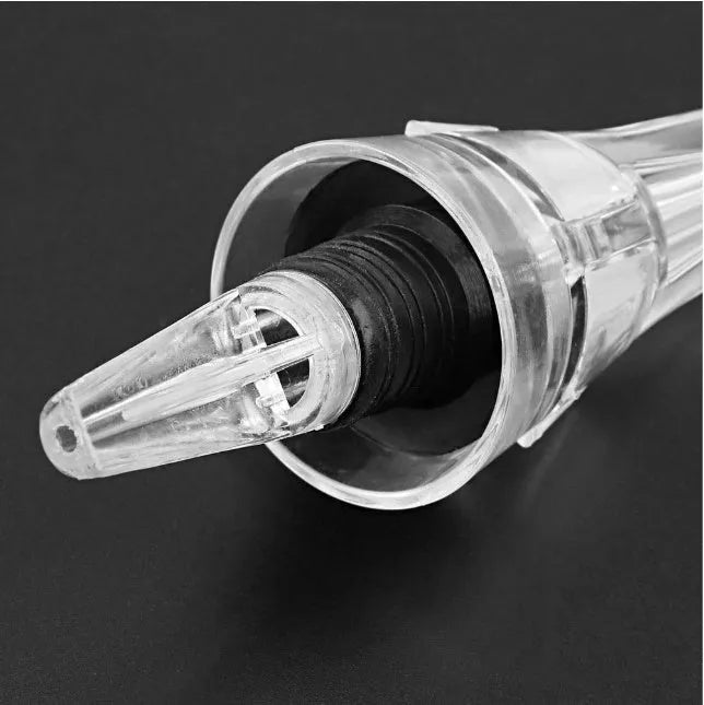 Compact clear acrylic wine aerator with a stainless steel filter insert on a wooden table.