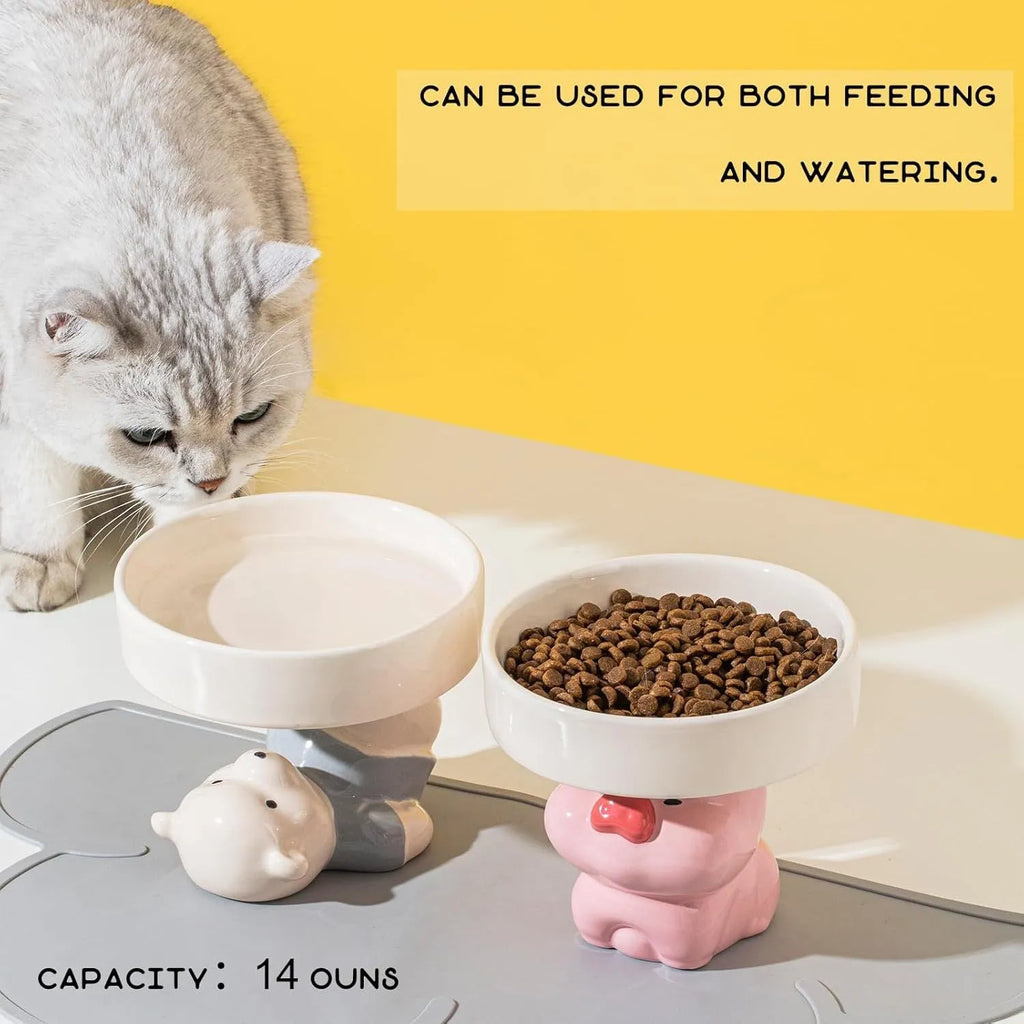 Raised ceramic cat bowl with animal design in pink, yellow, or white on a wooden floor.