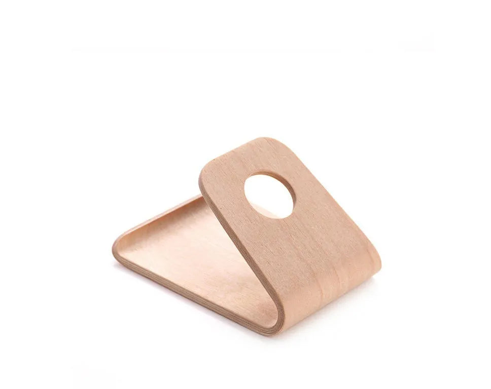 Handmade solid wood iPhone stand in walnut finish on a desk, holding a phone with a charging cable routed through the cable channel.