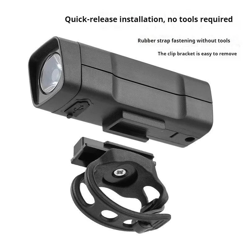 A black USB-rechargeable bicycle headlight mounted on a handlebar with a quick-release strap.