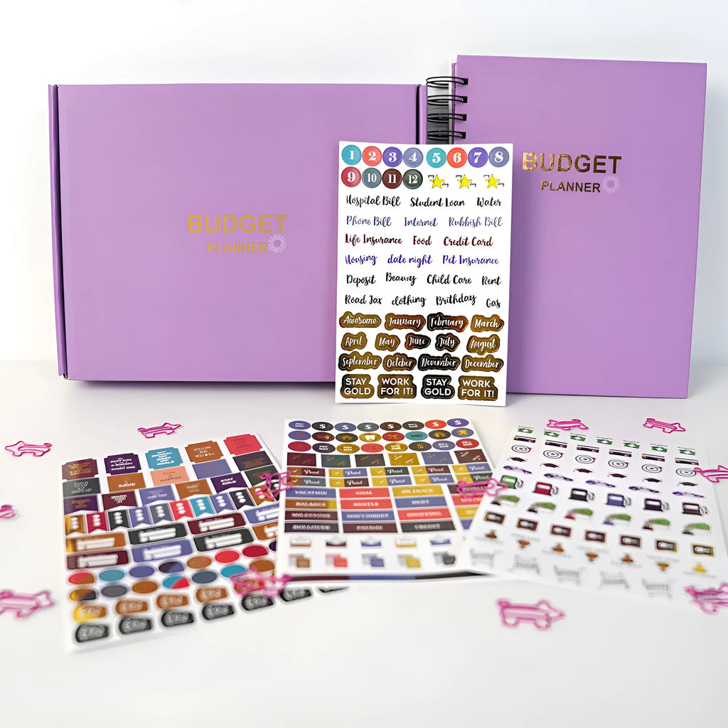 Purple coil-bound budget notebook open showing monthly planning pages with financial stickers and paper clips