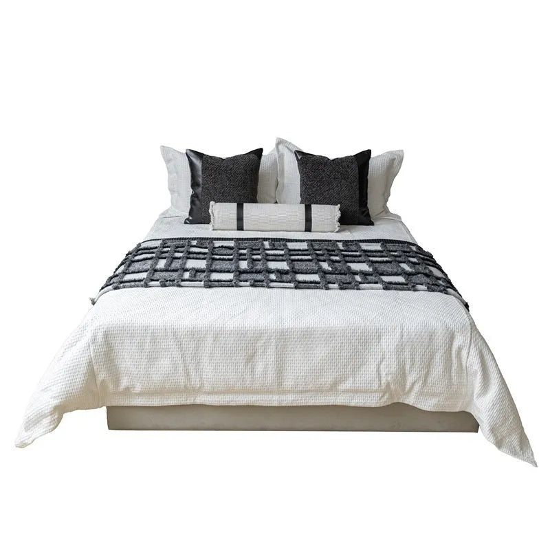 Grey and white plaid polyester bed runner blanket with matching pillowcase and leather round pillow on a double bed.