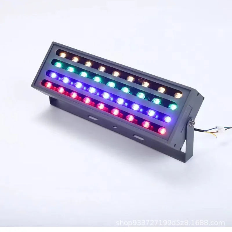 Silver aluminium outdoor LED spotlight projecting multi-coloured light onto trees.