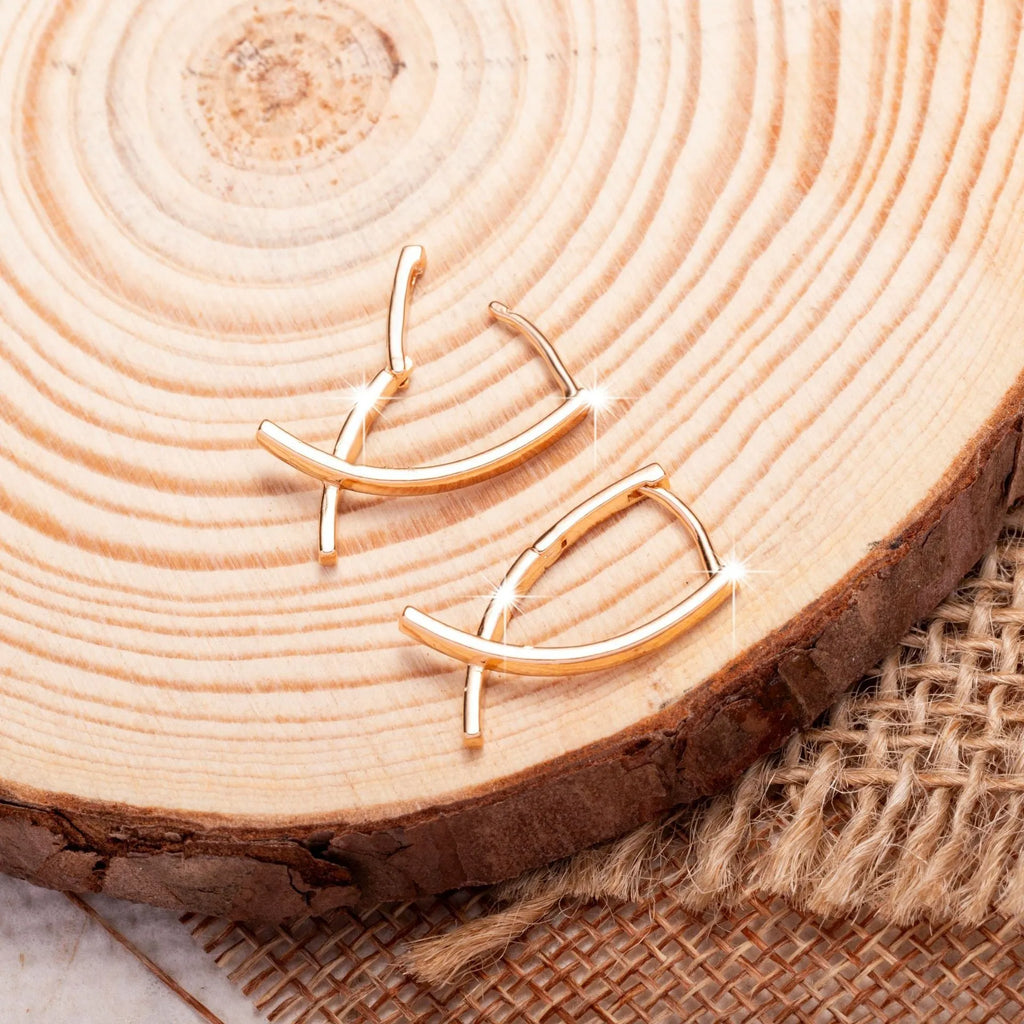 A pair of rose gold cross-shaped earrings made from copper on a white background.