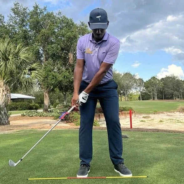 A plastic golf swing plane simulator training aid on a green background.