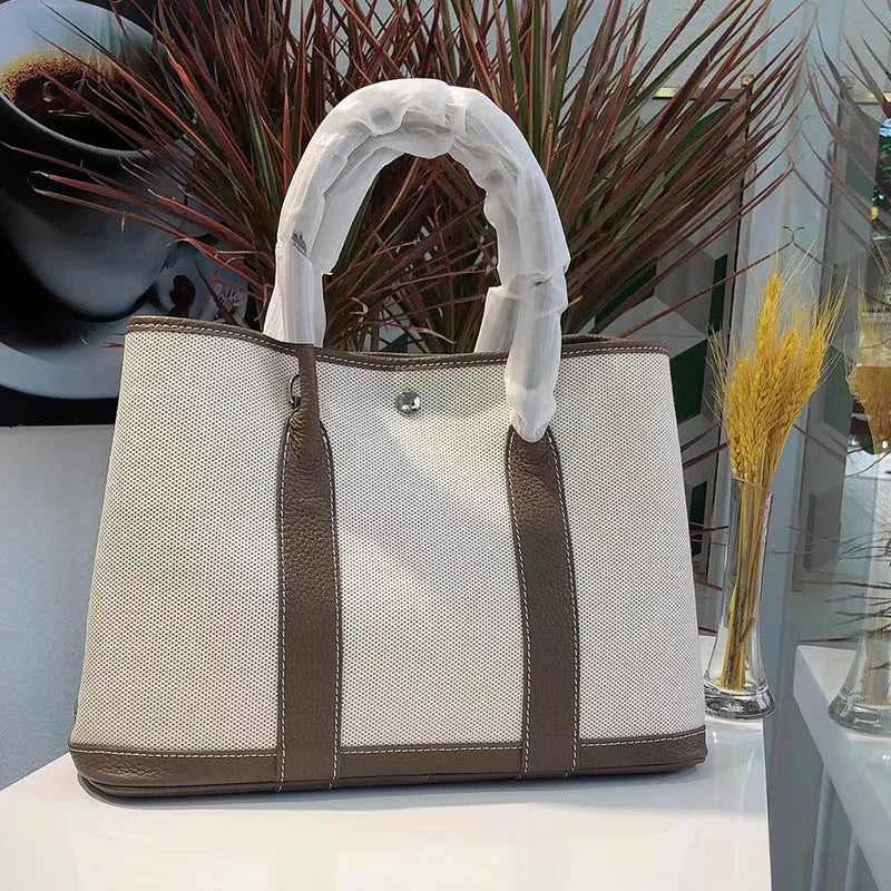 Women's canvas bucket tote bag with leather handles and detailing in black, shown with open top revealing internal zip pocket.