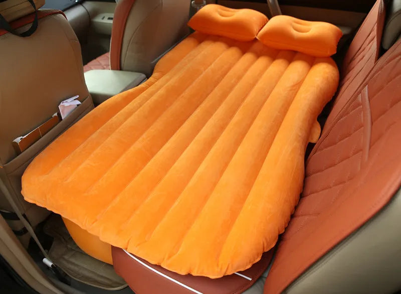 Black inflatable car bed with flocked surface and two pillows, shown inside a vehicle.