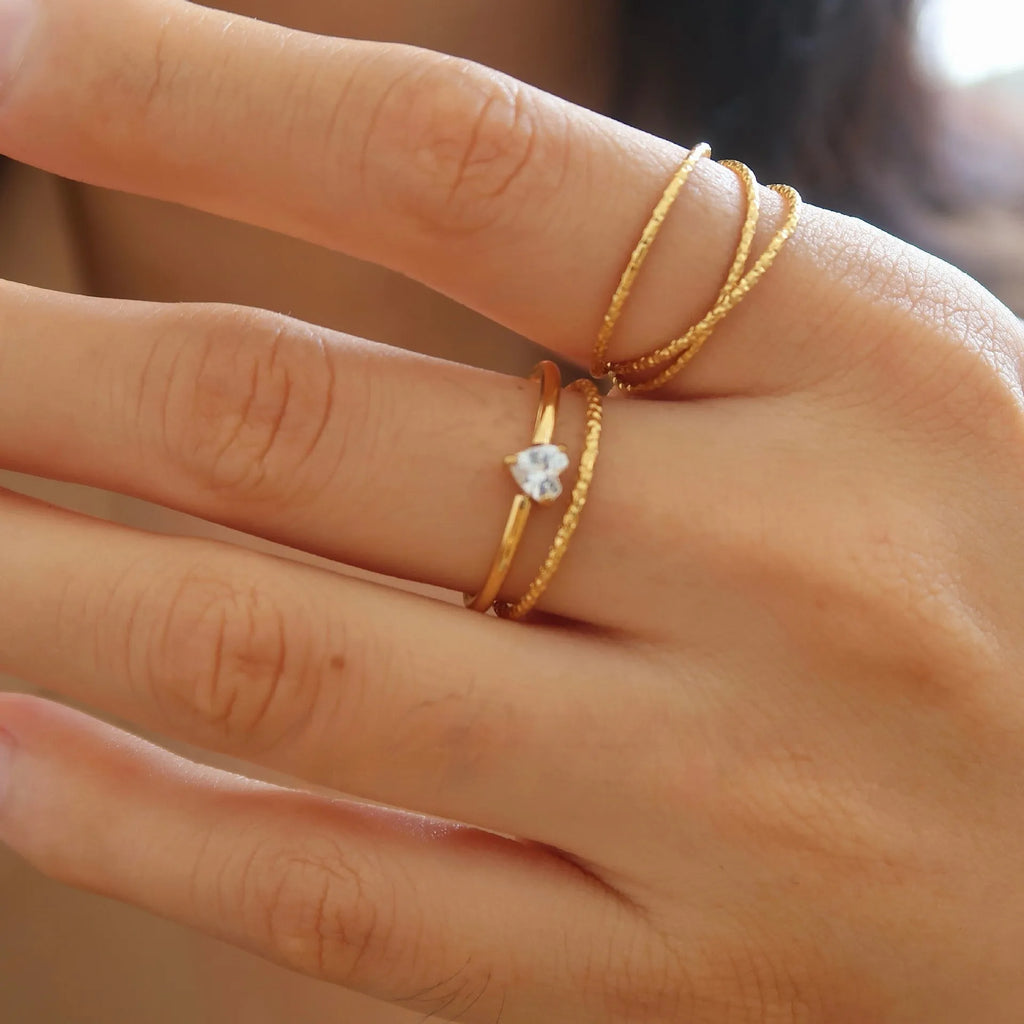Golden electroplated stainless steel love heart ring and oval ring for women on a plain background.